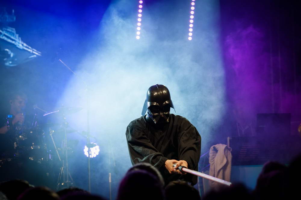 Sänger als Darth Vader verkleidet hält Leuchtschwert Richtung Publikum