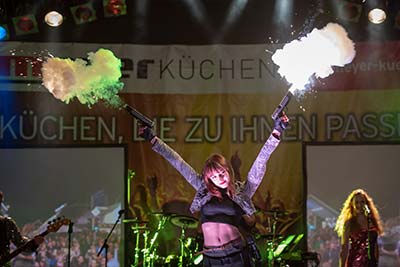 Sängerin der Band als Lara Croft verkleidet hält zwei Pistolen hoch aus denen ein Knalleffekt mit Rauch kommt